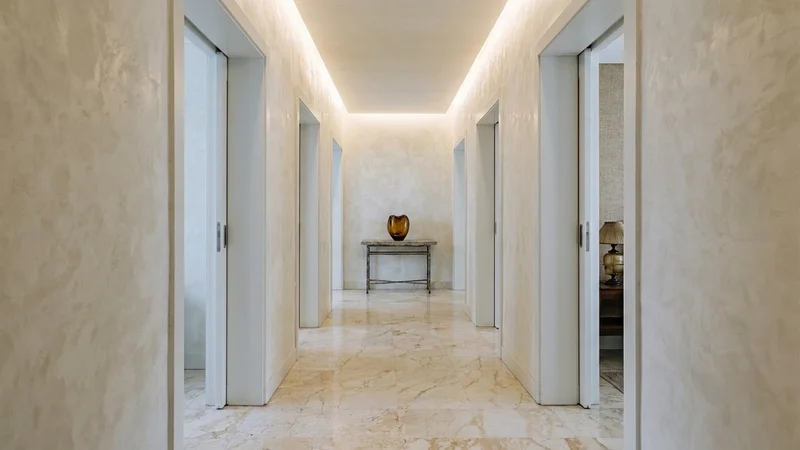 Pasillo de hotel boutique con proporciones generosas, techos altos y suelo de mármol crema